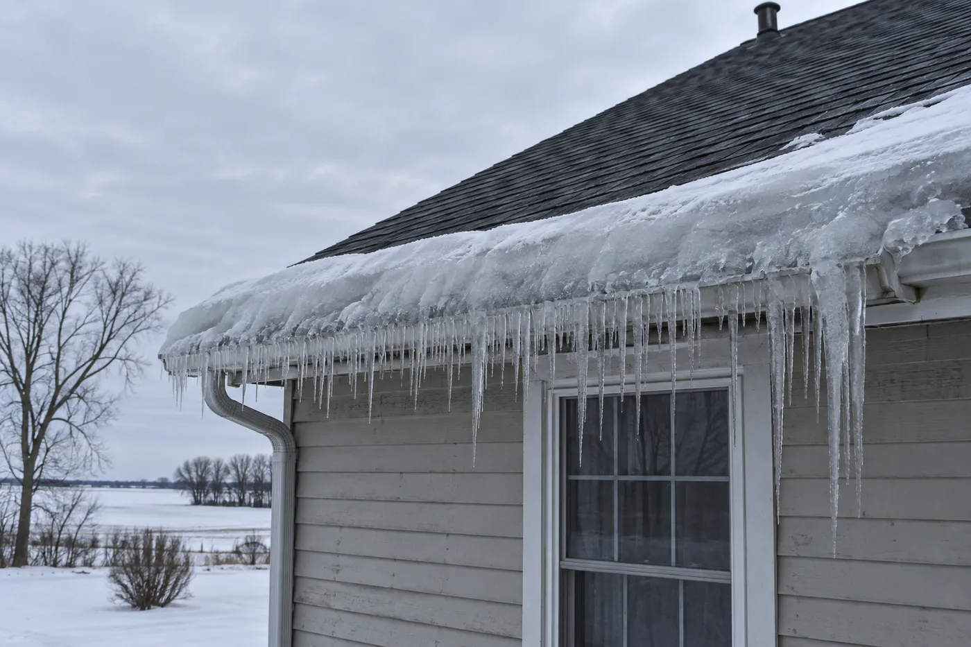 An ice dam and heavy icicles built up along a house eave in an eastern South Dakota winter, with the upper roof above it melted clear of snow.